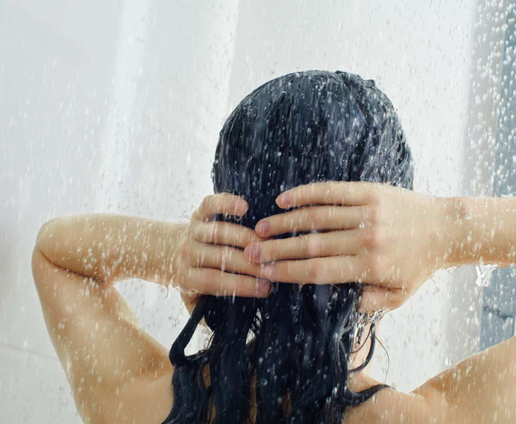 ragazza inquadrata da dietro doccia mentre lava i capelli